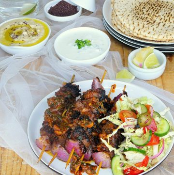 Grilled kangaroo skewers served with salad on white plate, flatbreads and condiments on the side