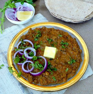 Lamb mince curry garnished with butter and onions and flatbreads on the side