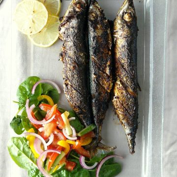 Three grilled sardines with salad and lemon slices