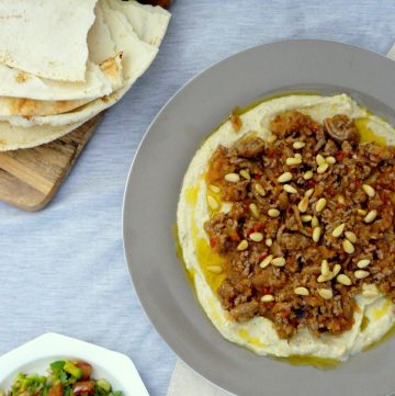 Hummus topped with minced lamb and pine nuts, pita bread and salad