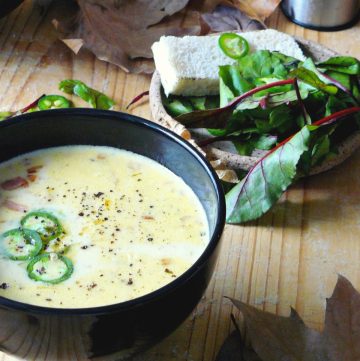 Beer and cheddar soup served in black bowl with bread and salad on the side