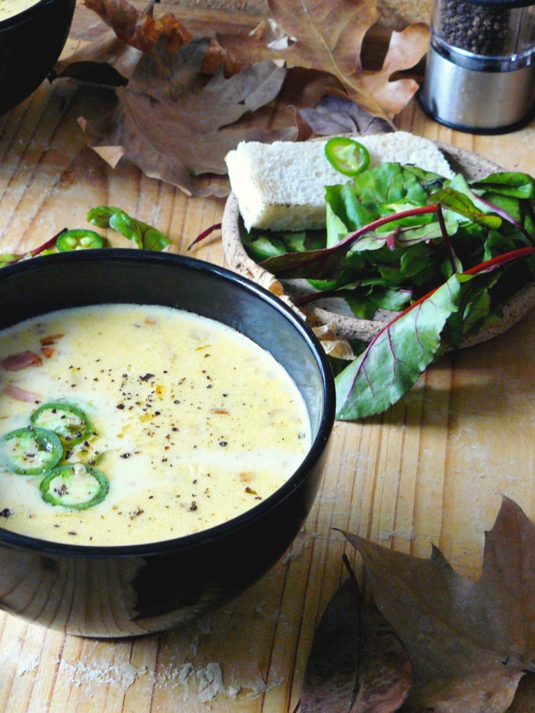 Beer and cheddar soup served in black bowl with bread and salad on the side