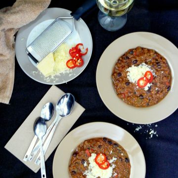 Two plates of beef chilli, a glass of white wine, cutlery and grated cheese on dining table