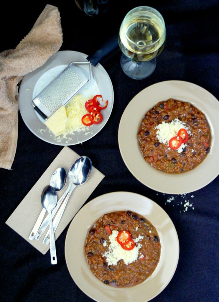 Two plates of beef chilli, a glass of white wine, cutlery and grated cheese on dining table