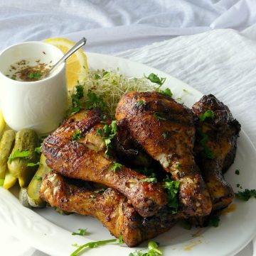 Grilled chicken drumsticks with pickled gherkins on white platter