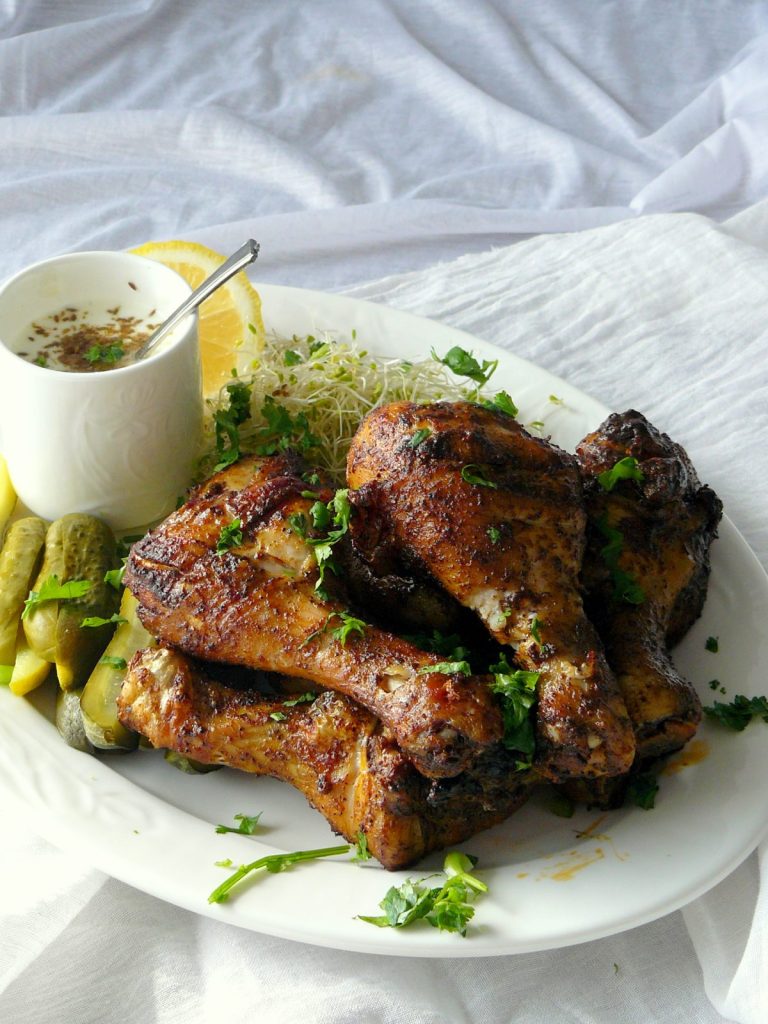 Grilled chicken drumsticks with pickled gherkins on white platter