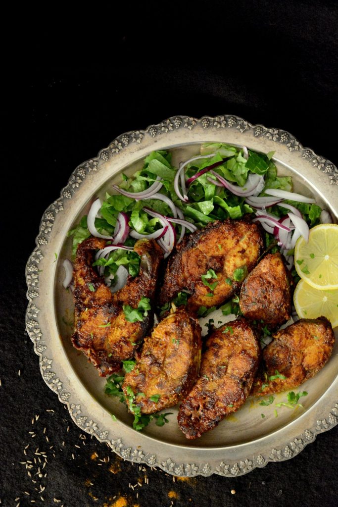 Fish fry slices on a silver platter with greens and lemon wedges