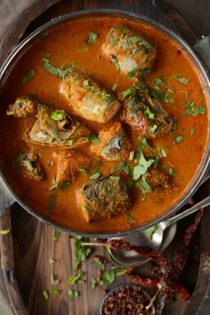 Indian fish curry in bowl with dry red chillies on the side