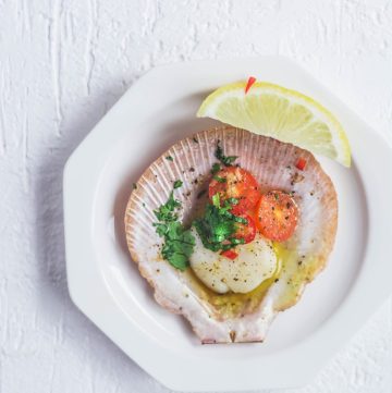 single scallop with butter and chillies on shell served in small white plate