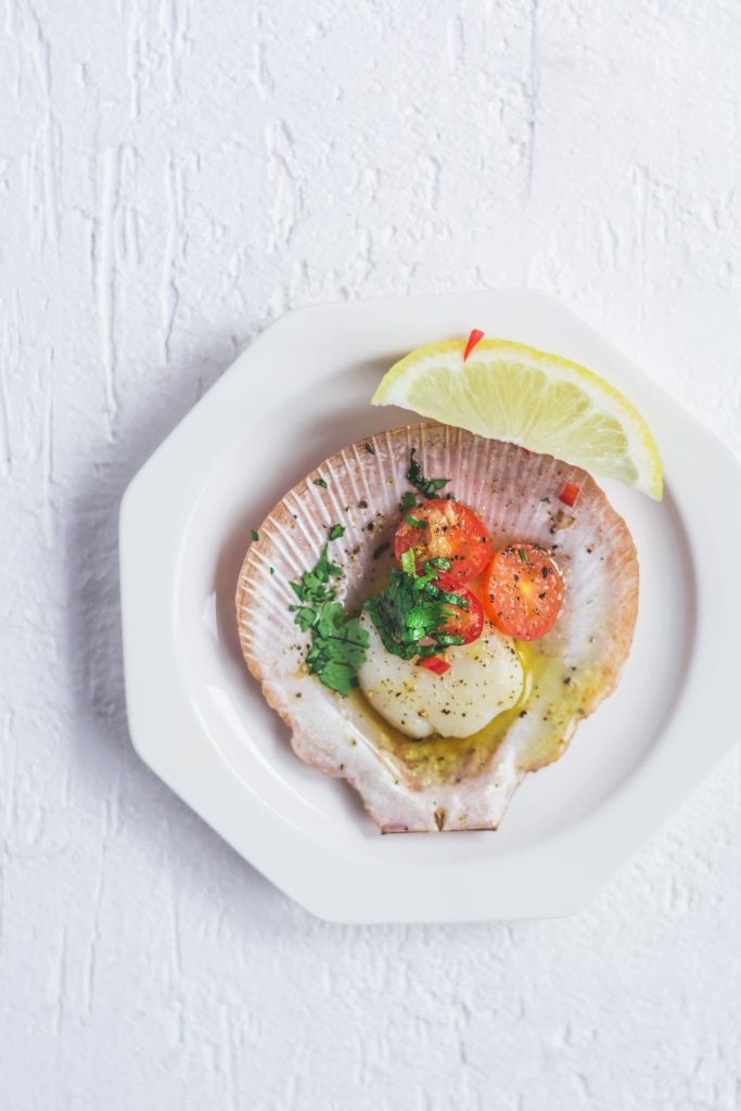 single scallop with butter and chillies on shell served in small white plate