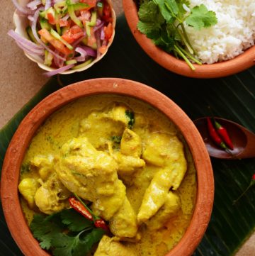 Chicken curry served in terracotta bowl with rice and salad on the side