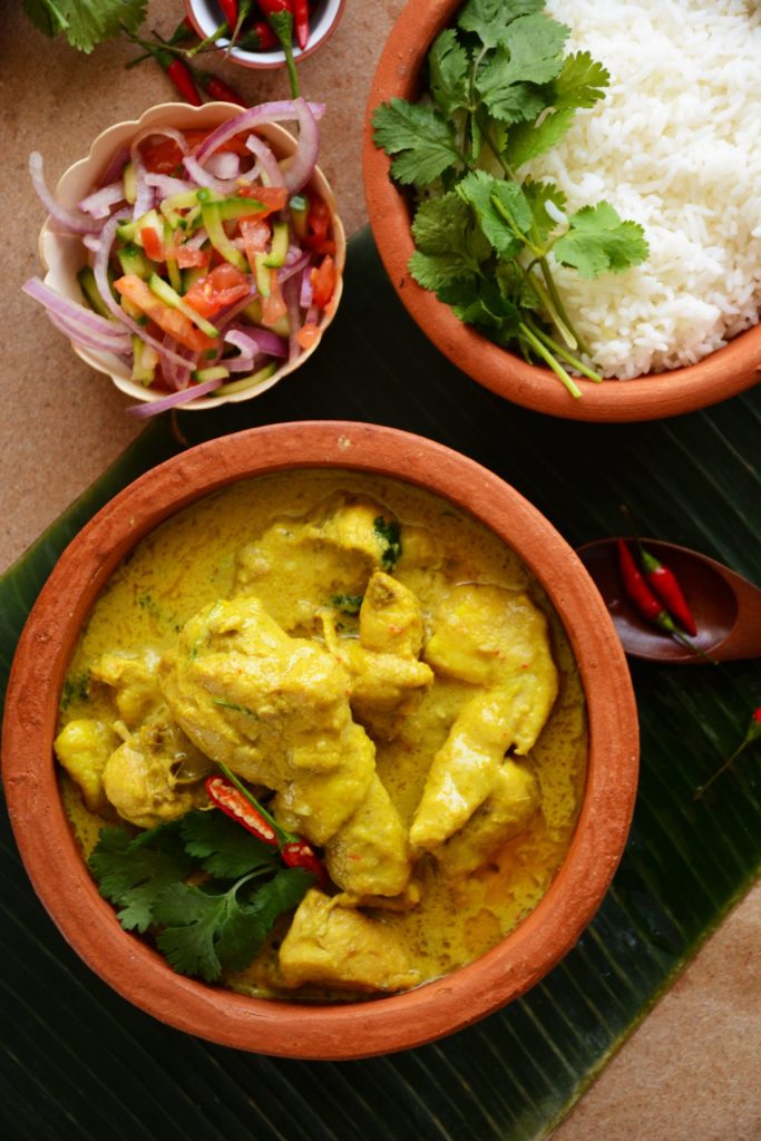 Chicken curry served in terracotta bowl with rice and salad on the side