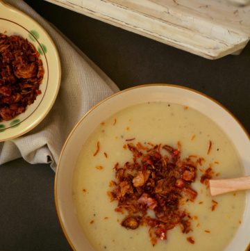 Potato cauliflower soup in bowl garnished with fried bacon and shallots