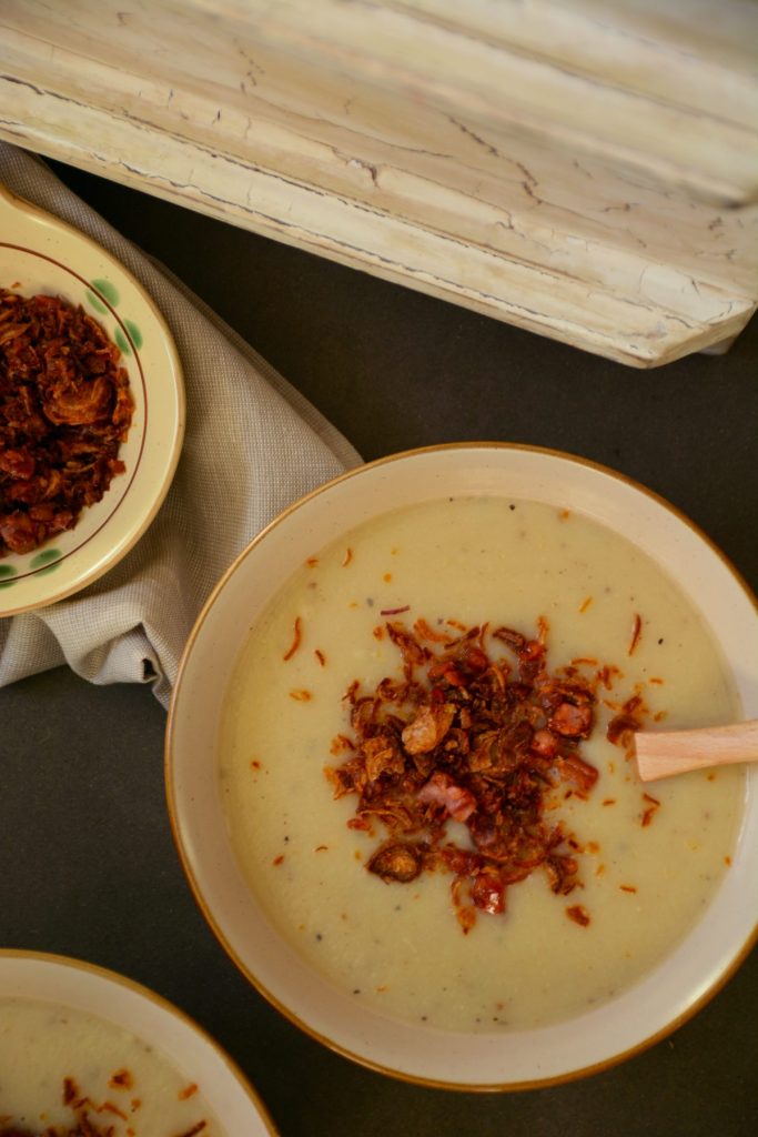 Potato cauliflower soup in bowl garnished with fried bacon and shallots