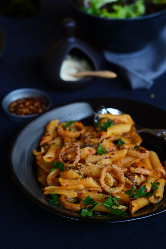 Pasta with squid in roasted tomato sauce served on black plate