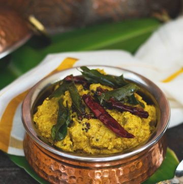 Copper pot with yellow vegetable curry garnished with dry red chilli