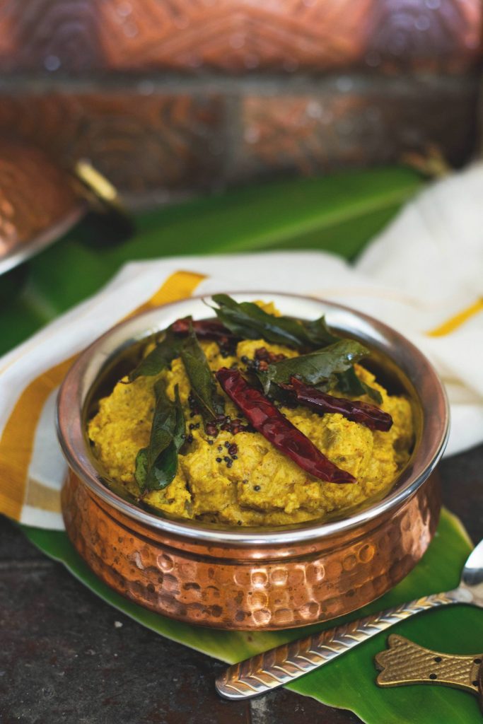Copper pot with yellow vegetable curry garnished with dry red chilli
