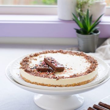 Icecream cake topped with chocolate shaving and biscuits on a cake stand