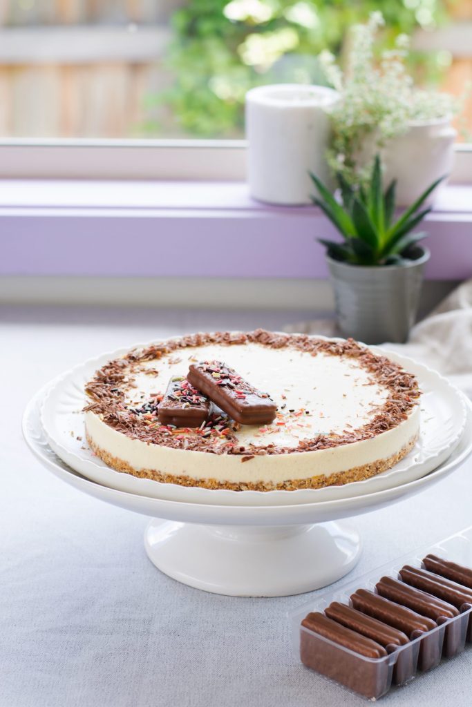 Icecream cake topped with chocolate shaving and biscuits on a cake stand