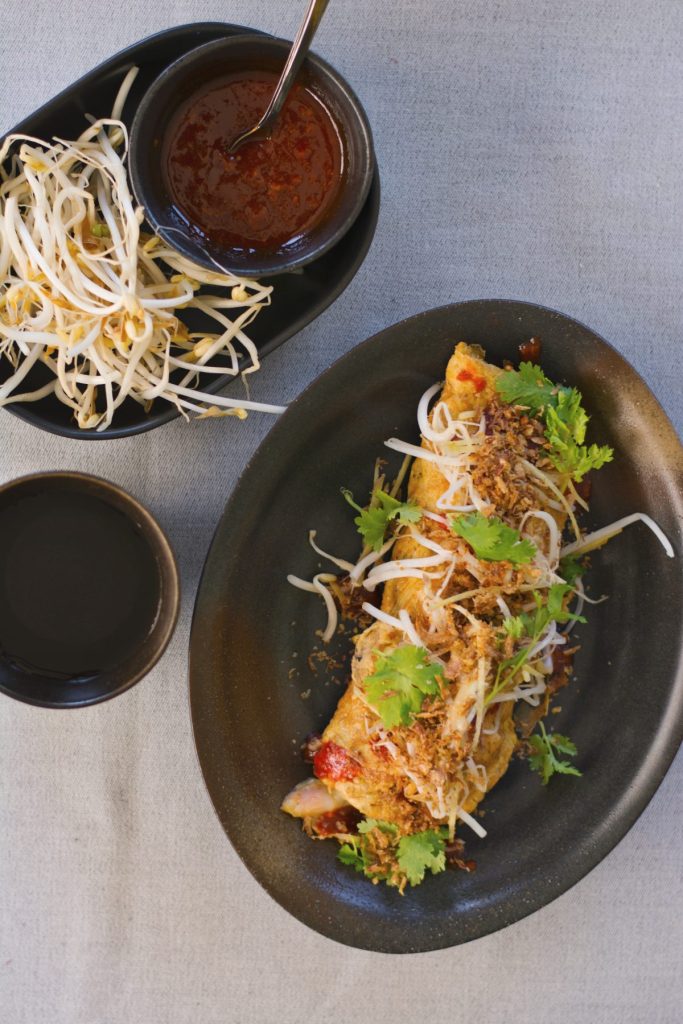 Stuffed prawn omelette served on oval shaped black plate with a side of bean sprouts