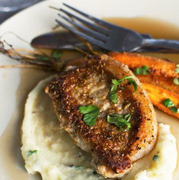 Grilled pork, mashed potatoes and carrots served on white plate with cutlery on the side