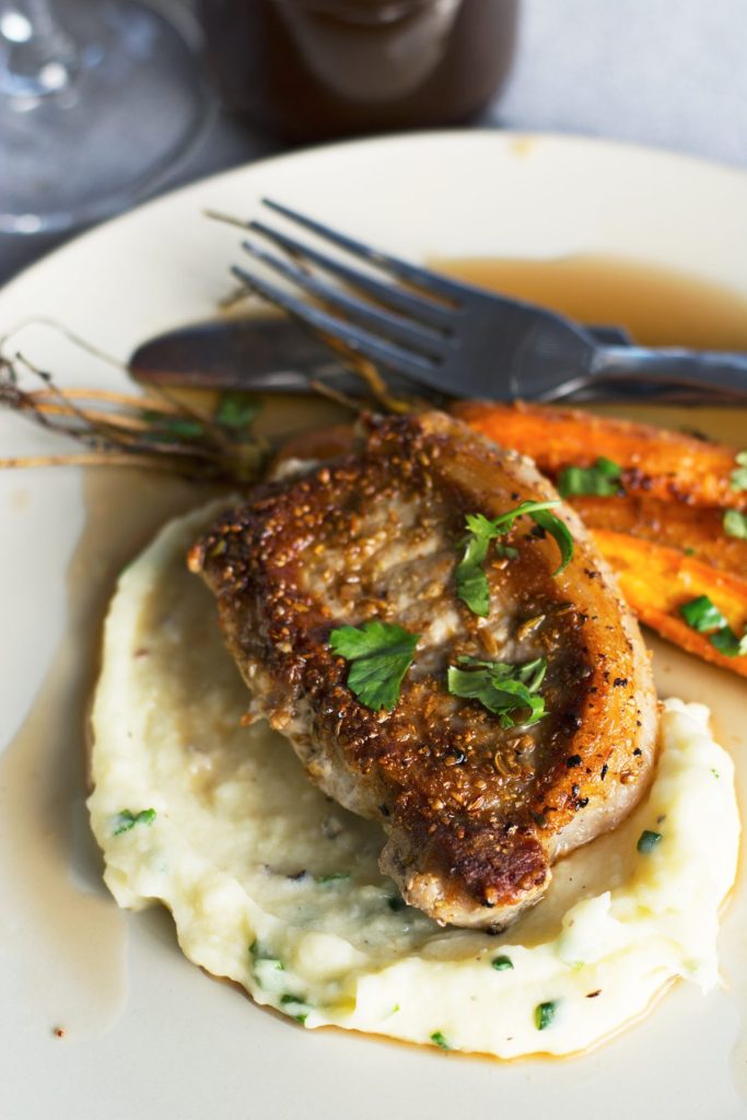 Grilled pork, mashed potatoes and carrots served on white plate with cutlery on the side