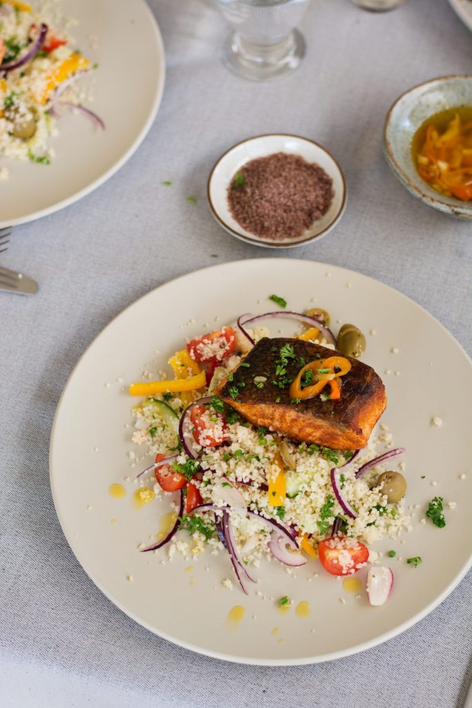 Fried salmon on top of couscous salad served on cream coloured plate