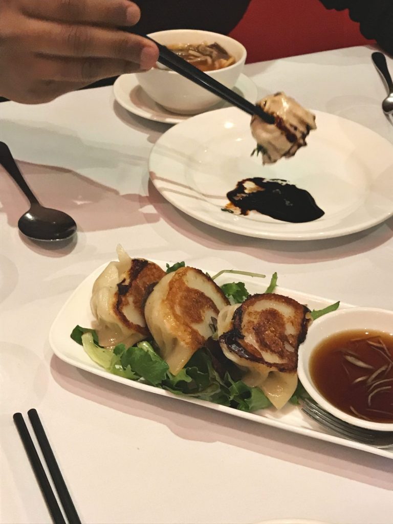 Three pan fried pork and prawn dumplings served on salad leaves in a white platter