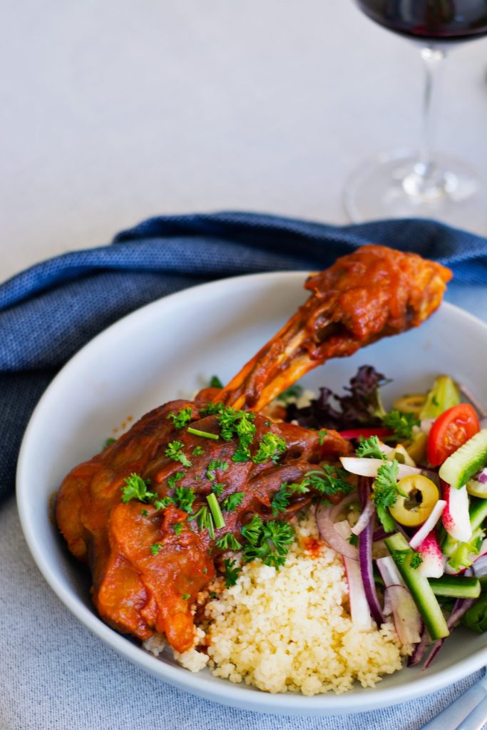 slow cooked lamb shank served with couscous and salad in blue bowl