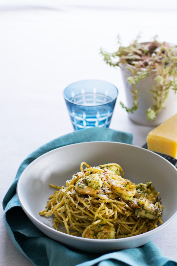 Spaghetti with prawns and pesto served in grey bowl with blue napkin on the side