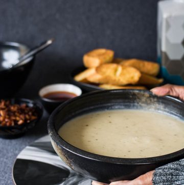 Hand holding potato parsnip soup in black bowl with toasted bread on the side