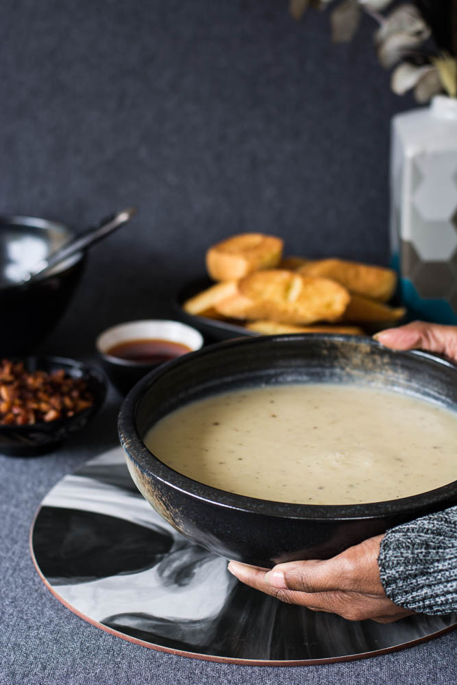 Hand holding potato parsnip soup in black bowl with toasted bread on the side