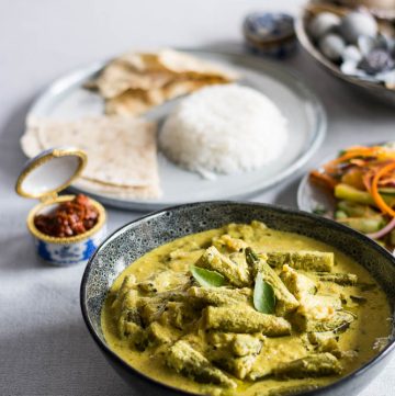 Indian okra curry with yoghurt in blue bowl with rice and flatbreads on the side