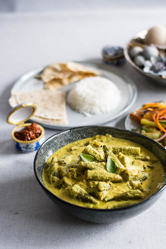 Indian okra curry with yoghurt in blue bowl with rice and flatbreads on the side