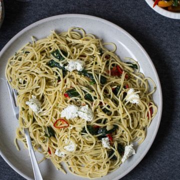 Spaghetti with spinach and goat's cheese on grey plate