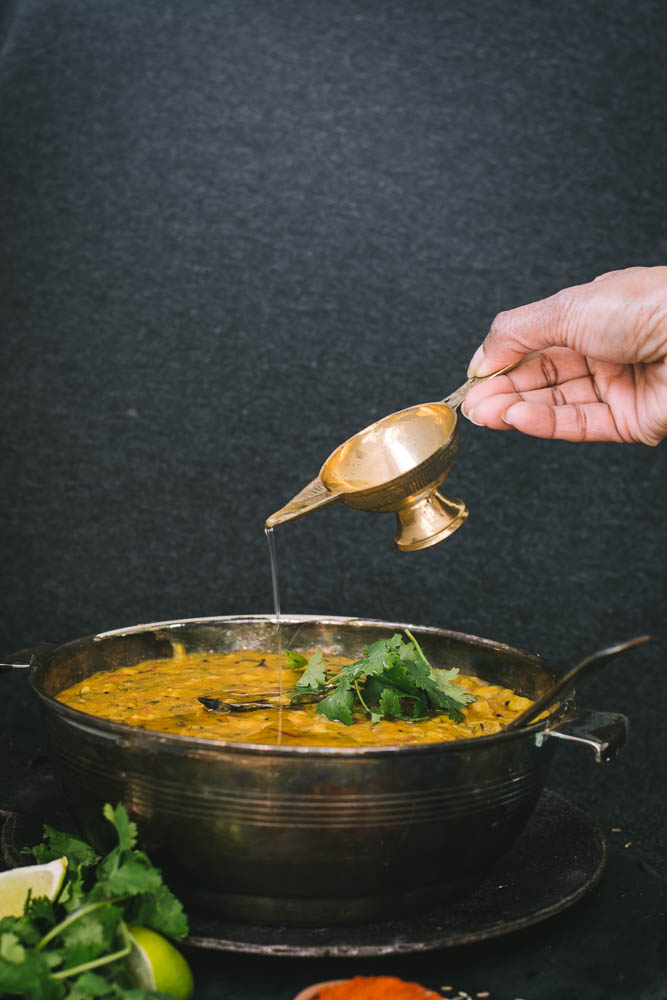 Hand pouring ghee on rice dish in bowl