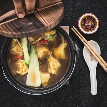 hand lifting lid of black bowl with chicken wonton soup