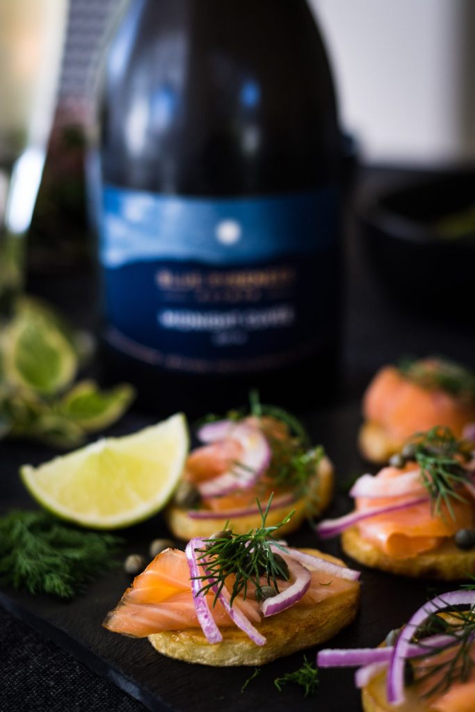 Close up of Potatoes topped with smoked salmon, capers, dill with wine bottle in background