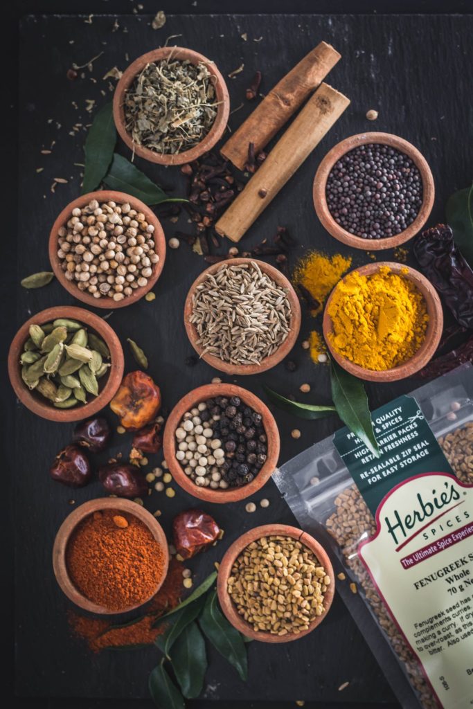 an array of whole spices in small earthenware bowls