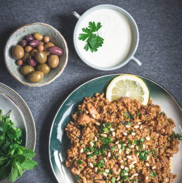 Freekeh chicken pilaf on green plate with olives and yoghurt on the side