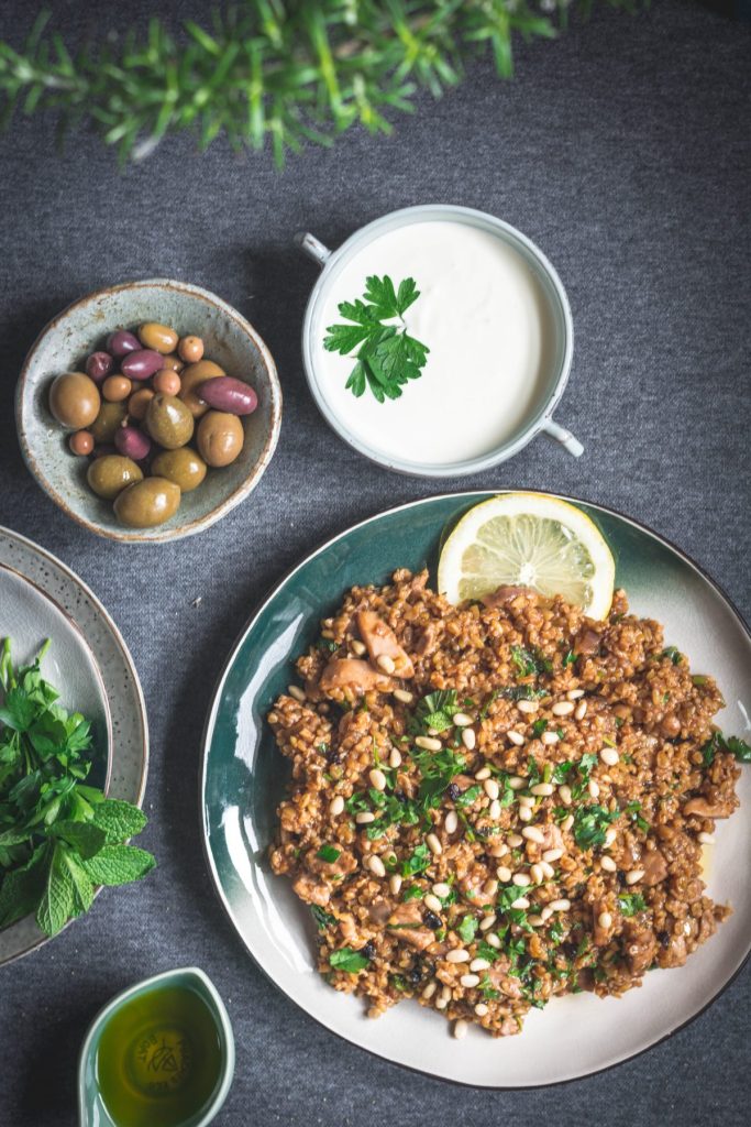 Freekeh chicken pilaf on green plate with olives and yoghurt on the side