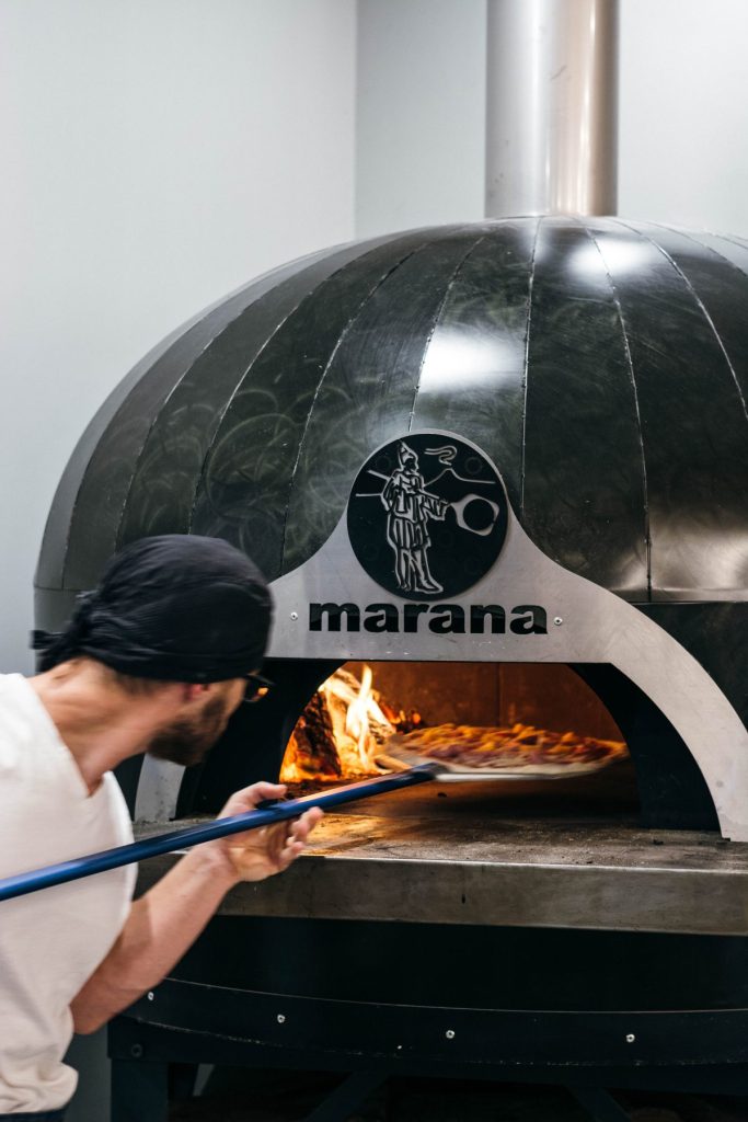 man placing pizza in woodfired oven