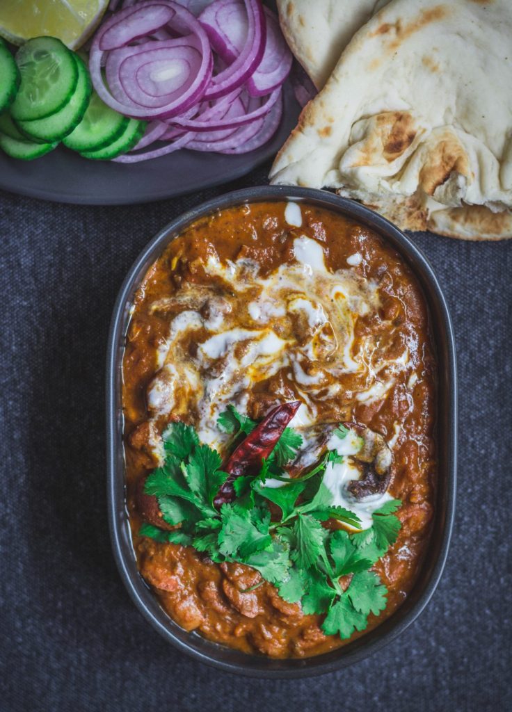 Indian style Borlotti beans curry in black bowl with flatbreads and salad on the side