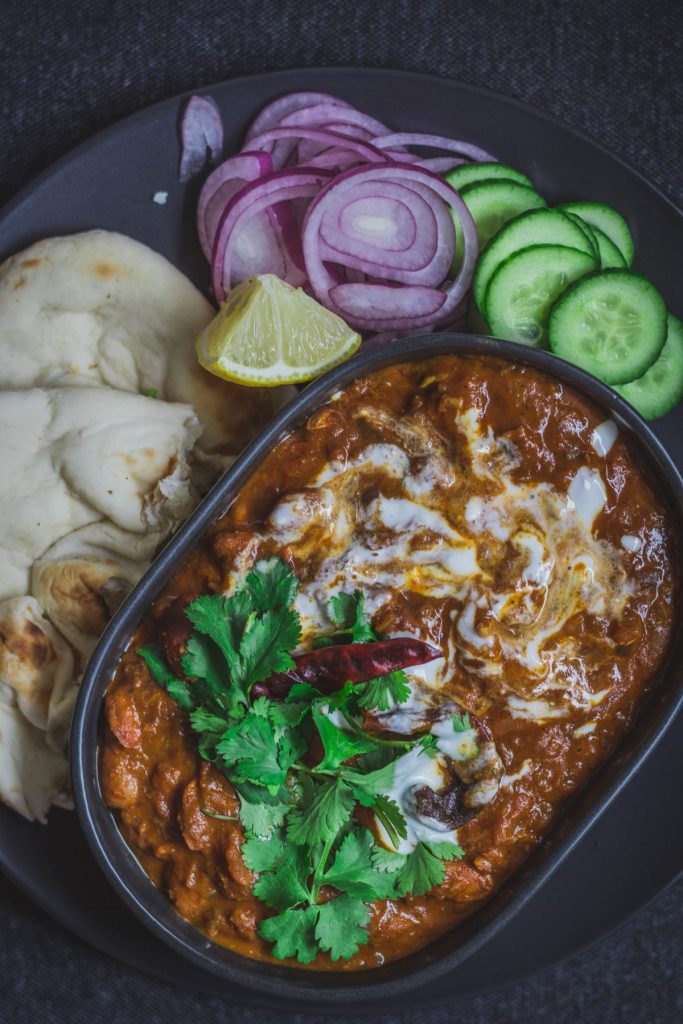 Indian style Borlotti beans curry in black bowl with flatbreads and salad on the side