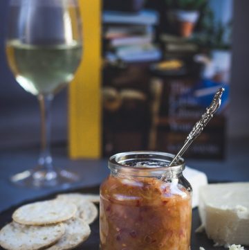 Cheese platter with a glass jar of apple, pear, chilli chutney and a glass of white wine on the side