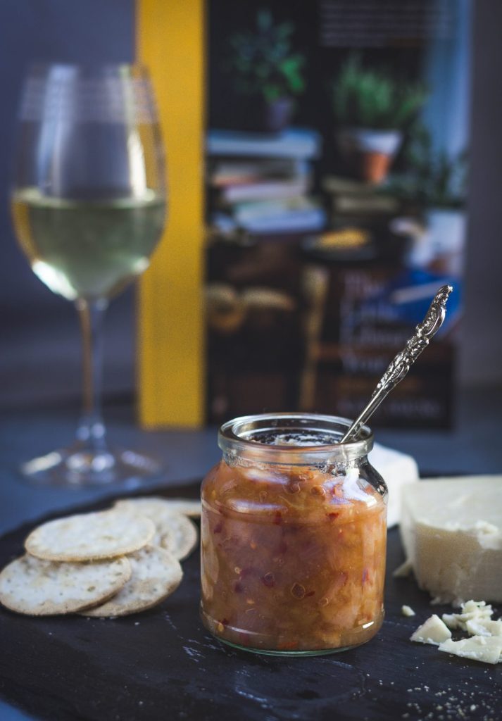 Cheese platter with a glass jar of apple, pear, chilli chutney and a glass of white wine on the side