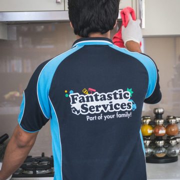 man from cleaning service cleaning kitchen cupboard