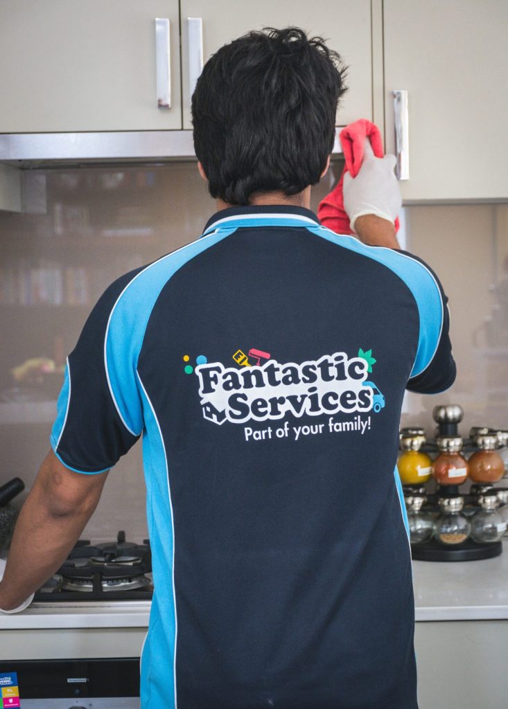 man from cleaning service cleaning kitchen cupboard