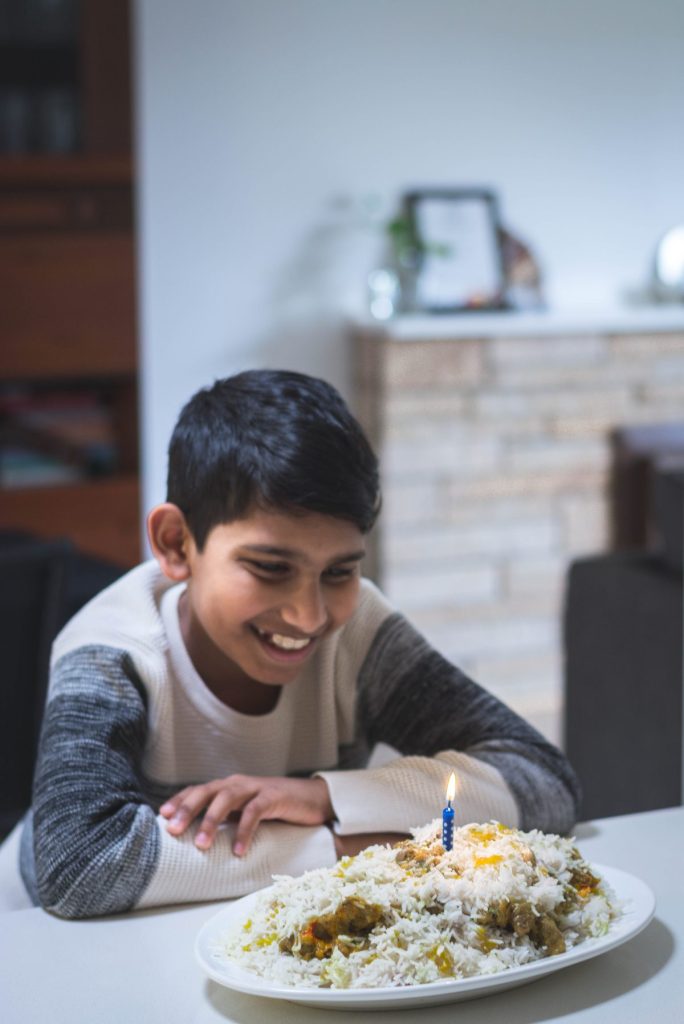 boy smiling at birthday candle on South Indian style mutton biryani on oval white platter