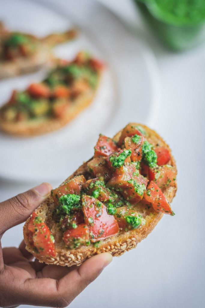 hand holding bruschetta with tomatoes and pesto